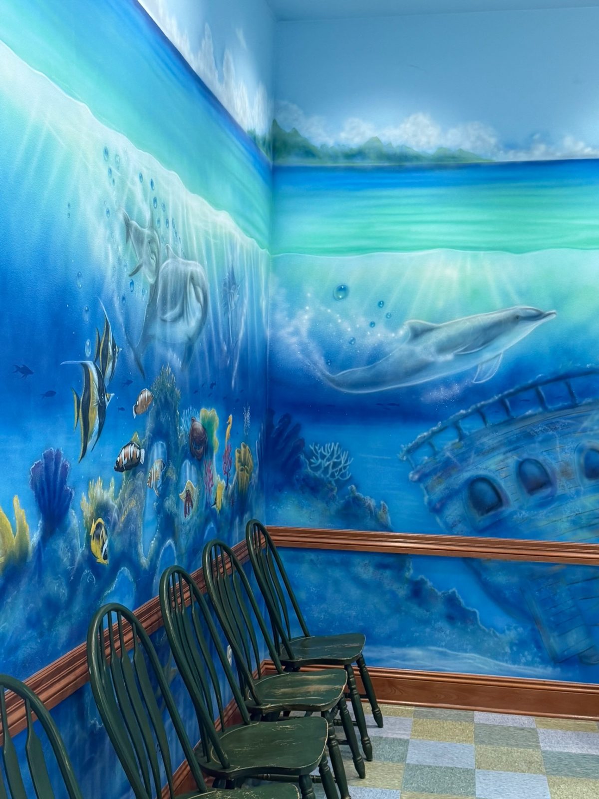The ocean-themed waiting area at Preferred Pediatrics, with dolphin murals and green wooden chairs