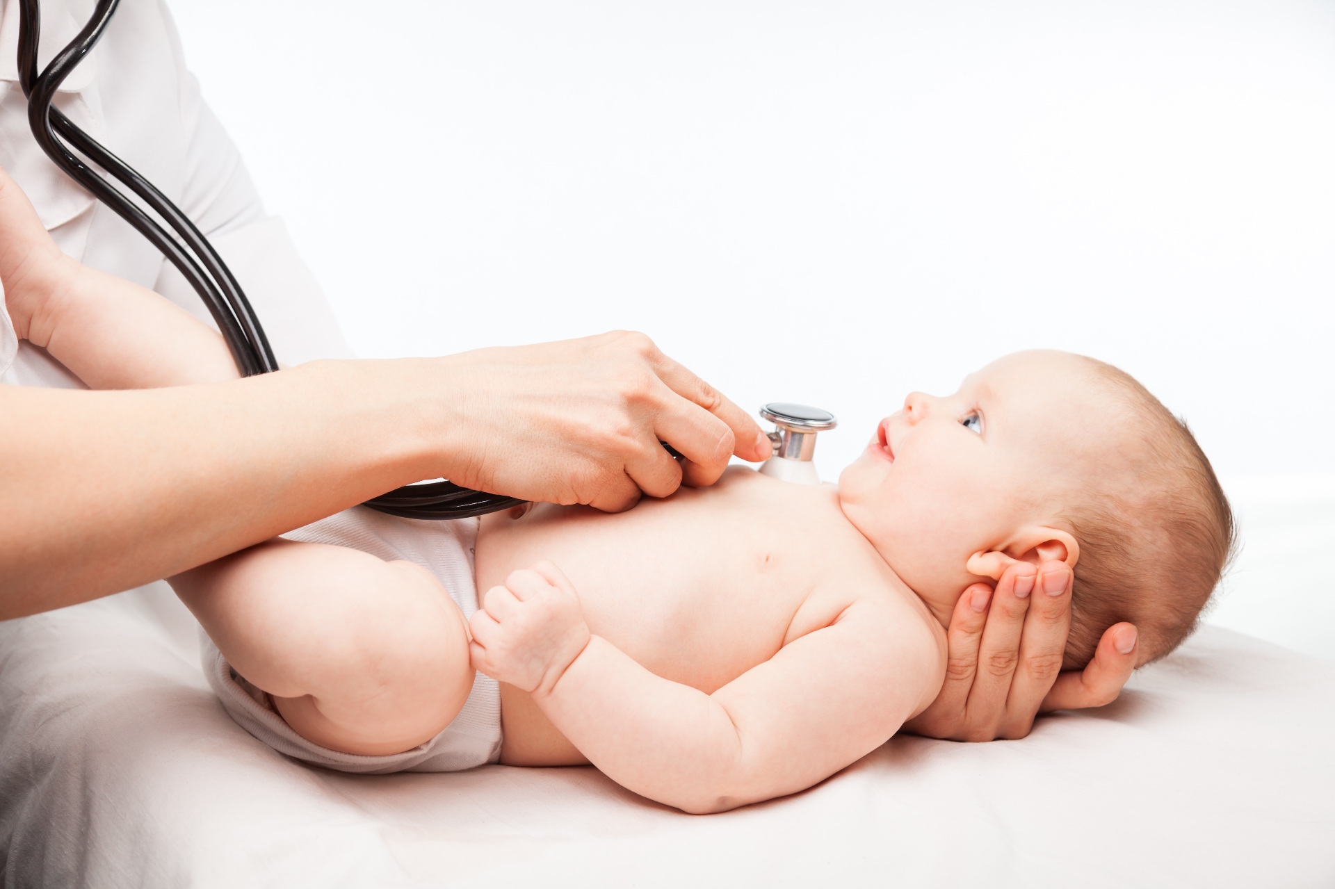 A pediatric provider listening to a smiling baby's heart with a stethoscope during a newborn checkup