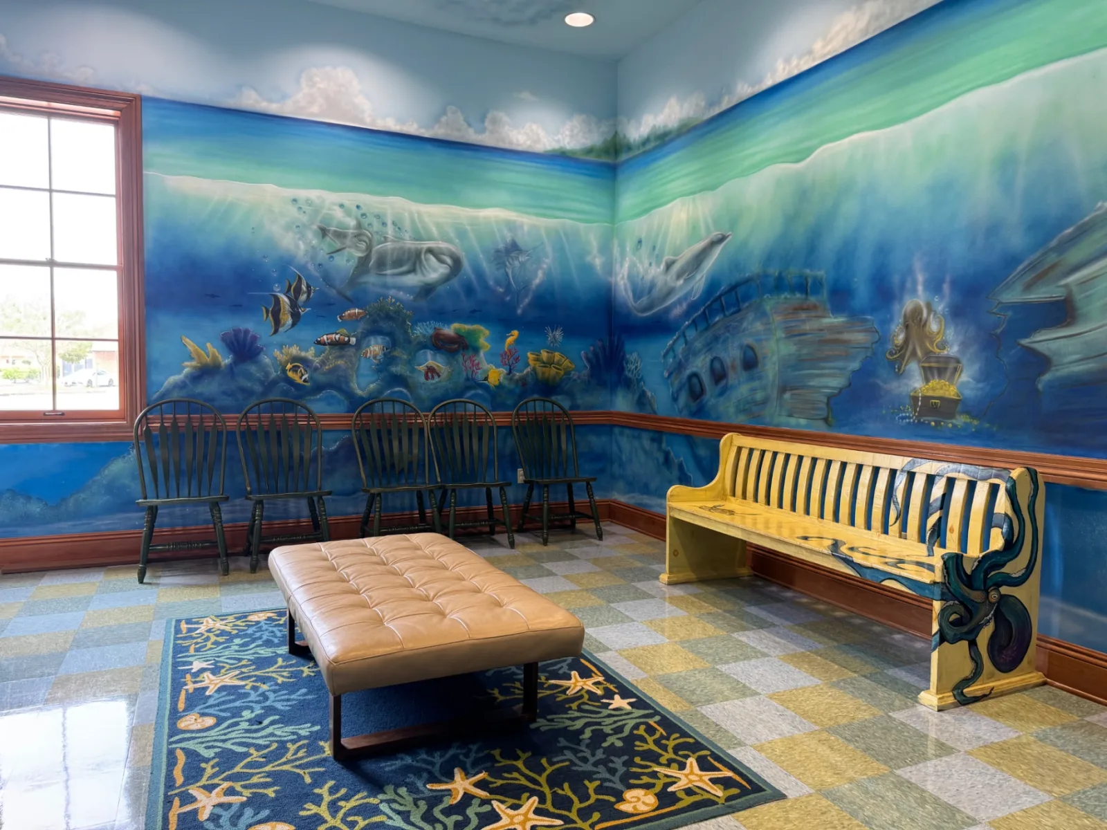 The ocean-themed waiting room at Preferred Pediatrics, with a hand-painted underwater mural of dolphins and a shipwreck behind a row of chairs