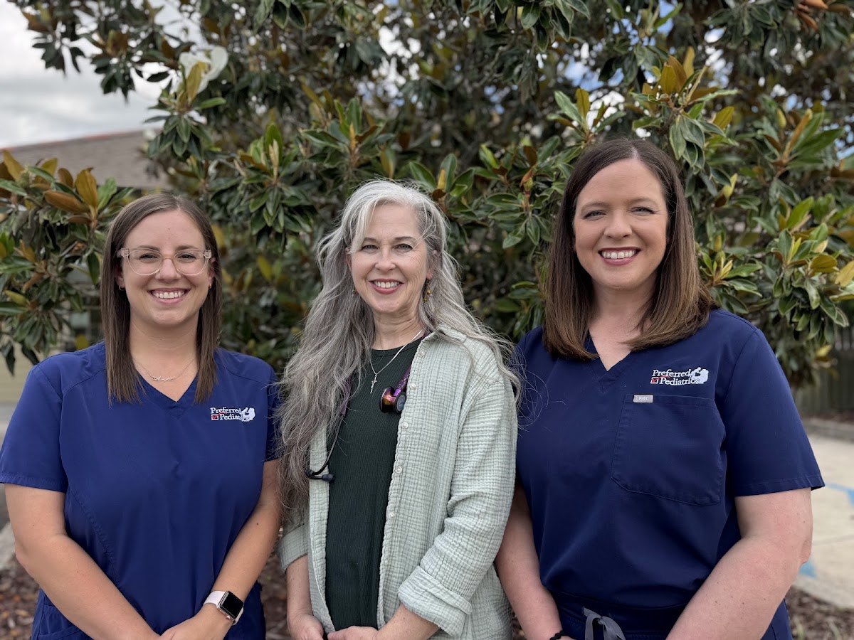 Three Preferred Pediatrics providers in navy scrubs smiling in front of a magnolia tree outside the clinic