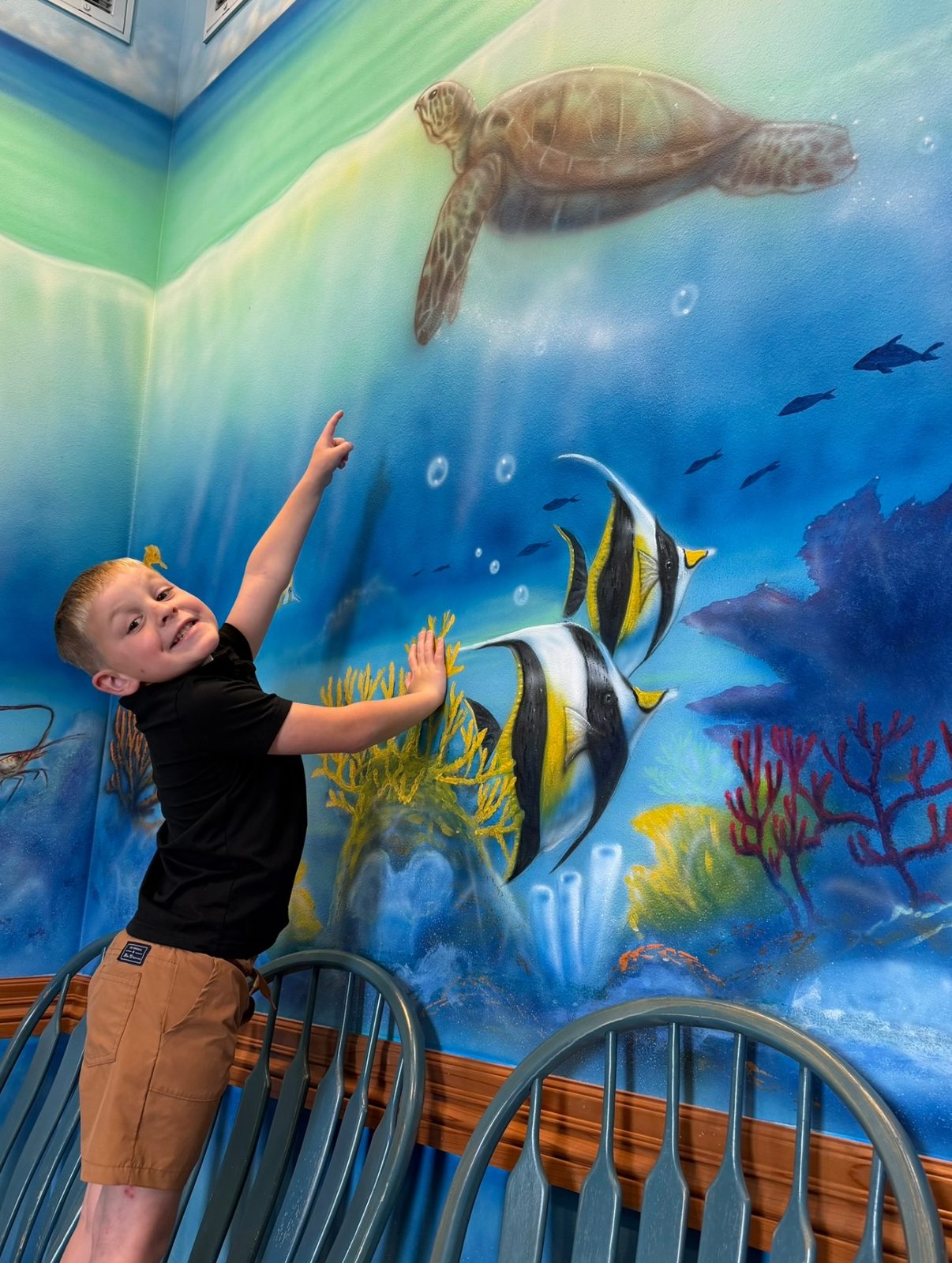 A young patient pointing at the painted sea turtle on the ocean mural at Preferred Pediatrics